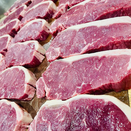 food_yard2 Close-up view of multiple fresh raw beef steaks arranged neatly in rows, showcasing their rich red color and marbled texture with a strip of white fat along the edge.