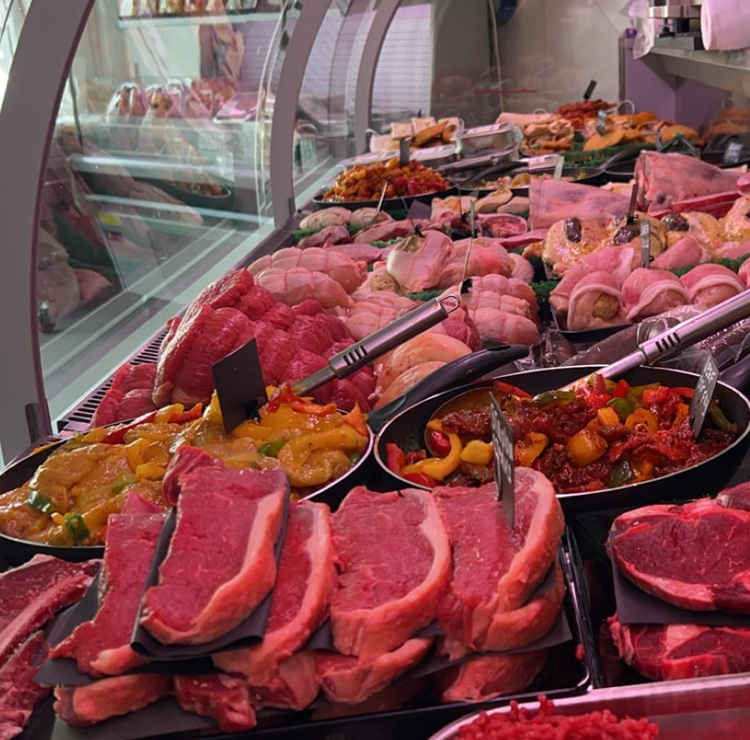 Close-up view of multiple fresh raw beef steaks arranged neatly in rows, showcasing their rich red color and marbled texture with a strip of white fat along the edge.